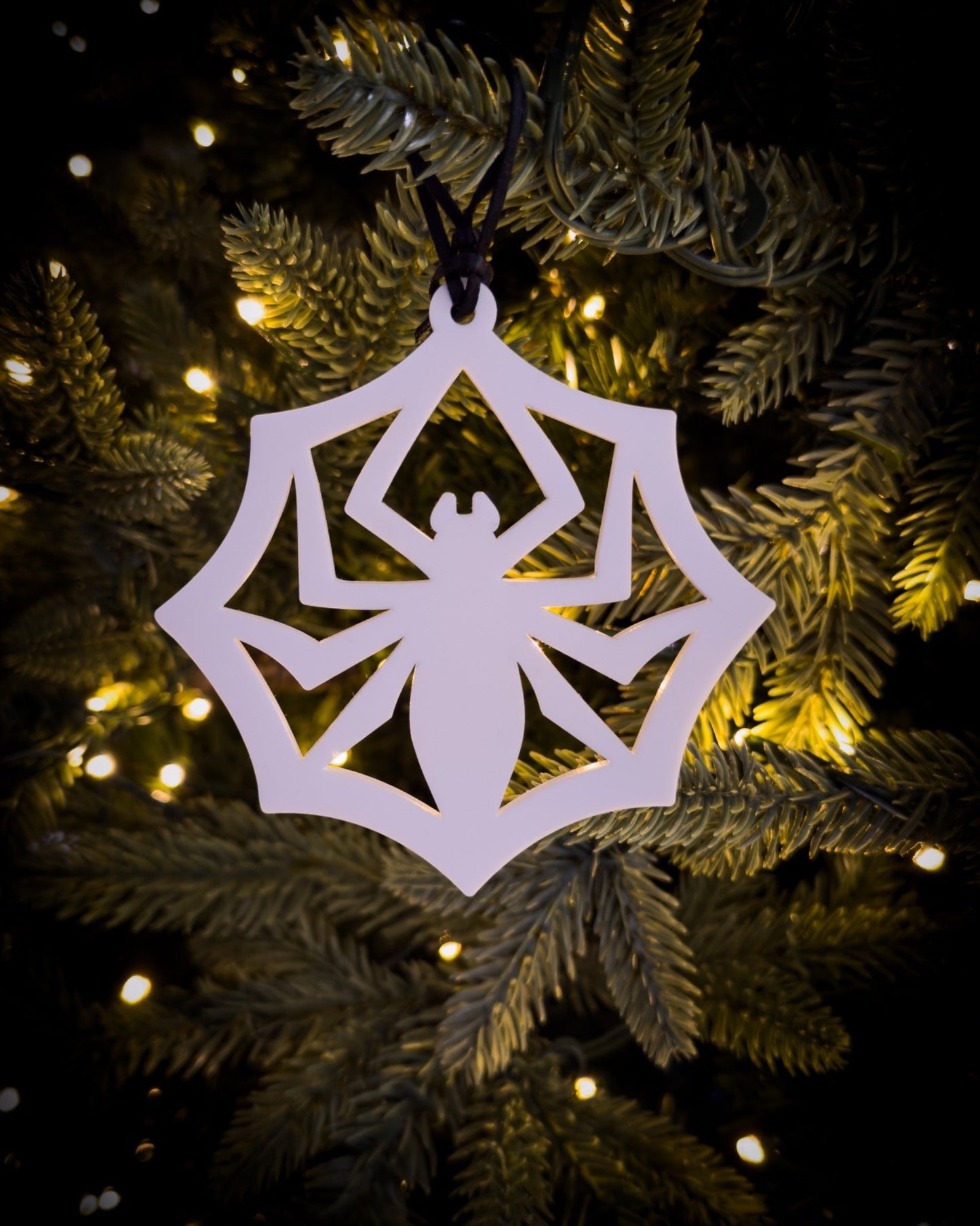 White acrylic, gothic spider web ornament hanging on Christmas tree with warm lights