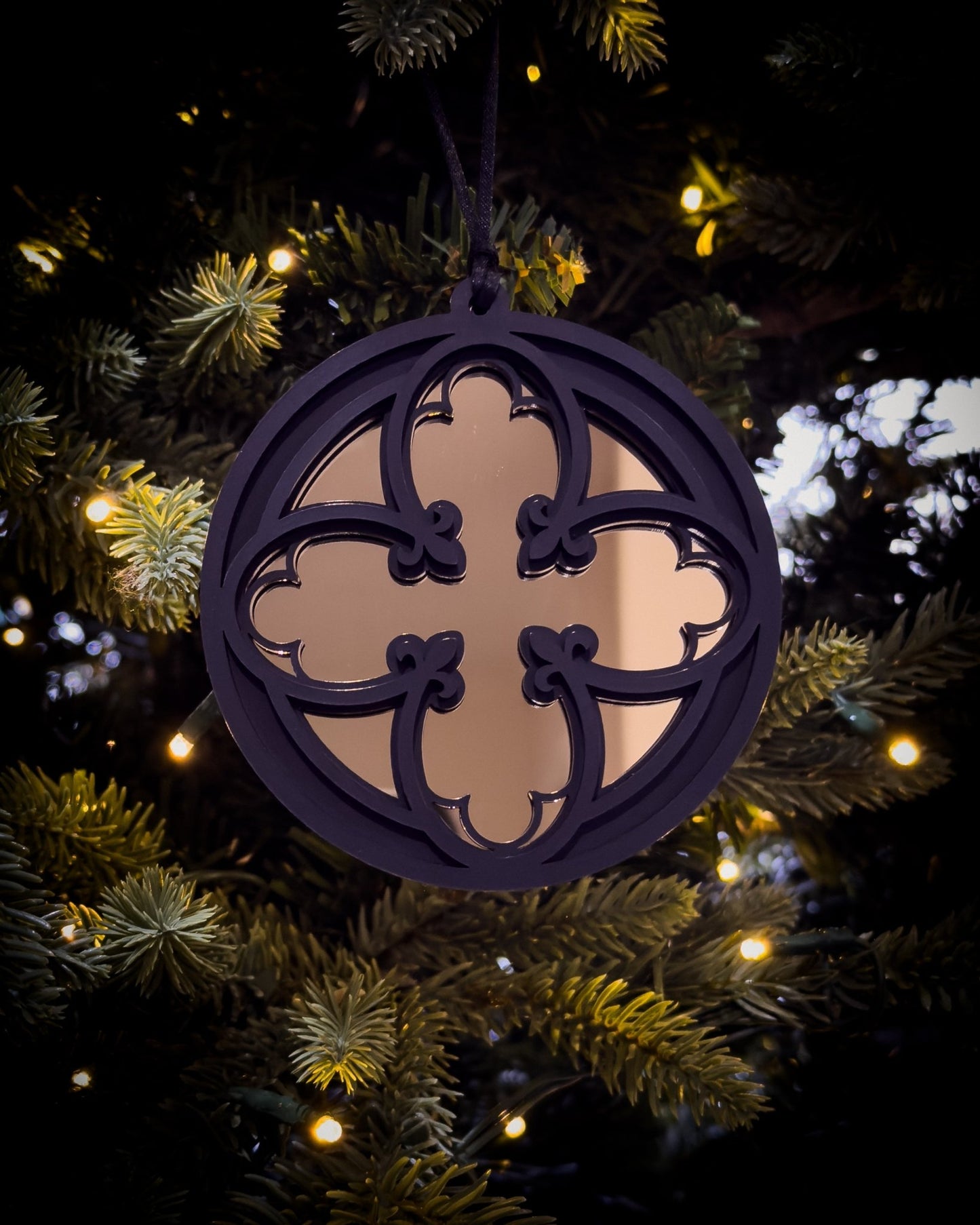 Gold gothic cathedral quatrefoil ornament hanging on Christmas tree with warm lights