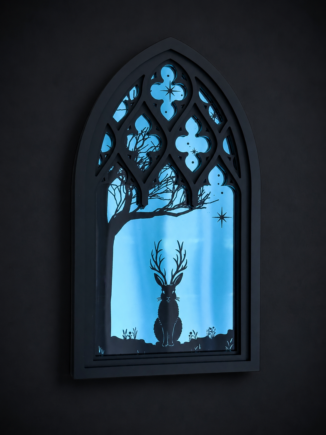 Gothic-style Cathedral window with blue silhouette of a Jackalope and tree against a dark mirror background