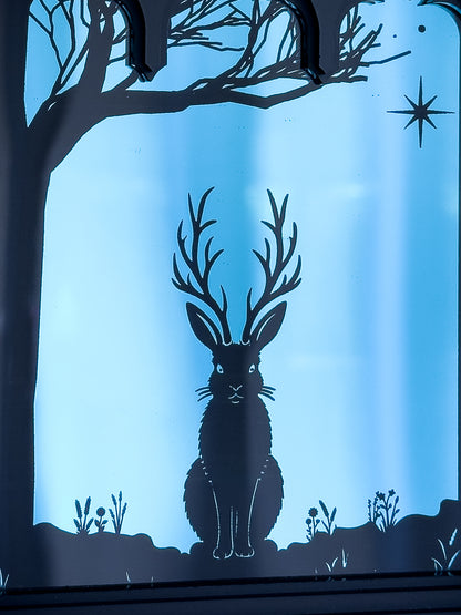 Close up of Gothic Cathedral window with blue silhouette of a Jackalope and tree against a dark mirror background