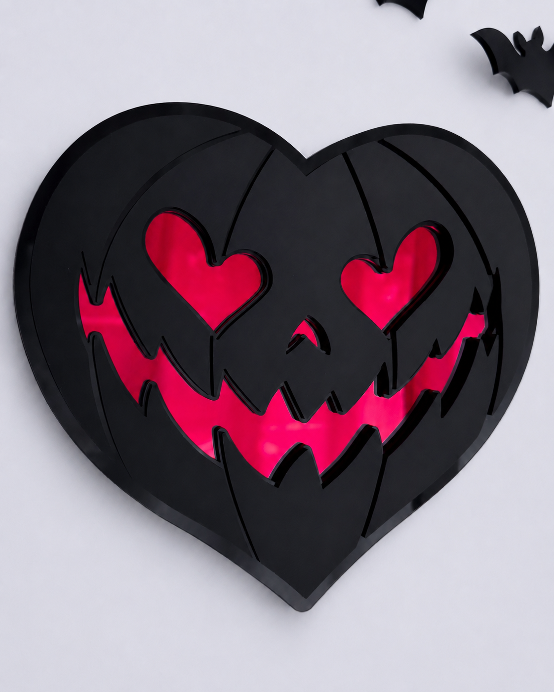 Black heart-shaped pumpkin wall art with red mirrored eyes and smile on a bright cool-toned wall.