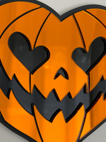 Close up view of orange heart-shaped pumpkin mirror wall art in layered black acrylic on a bright cool-toned wall.