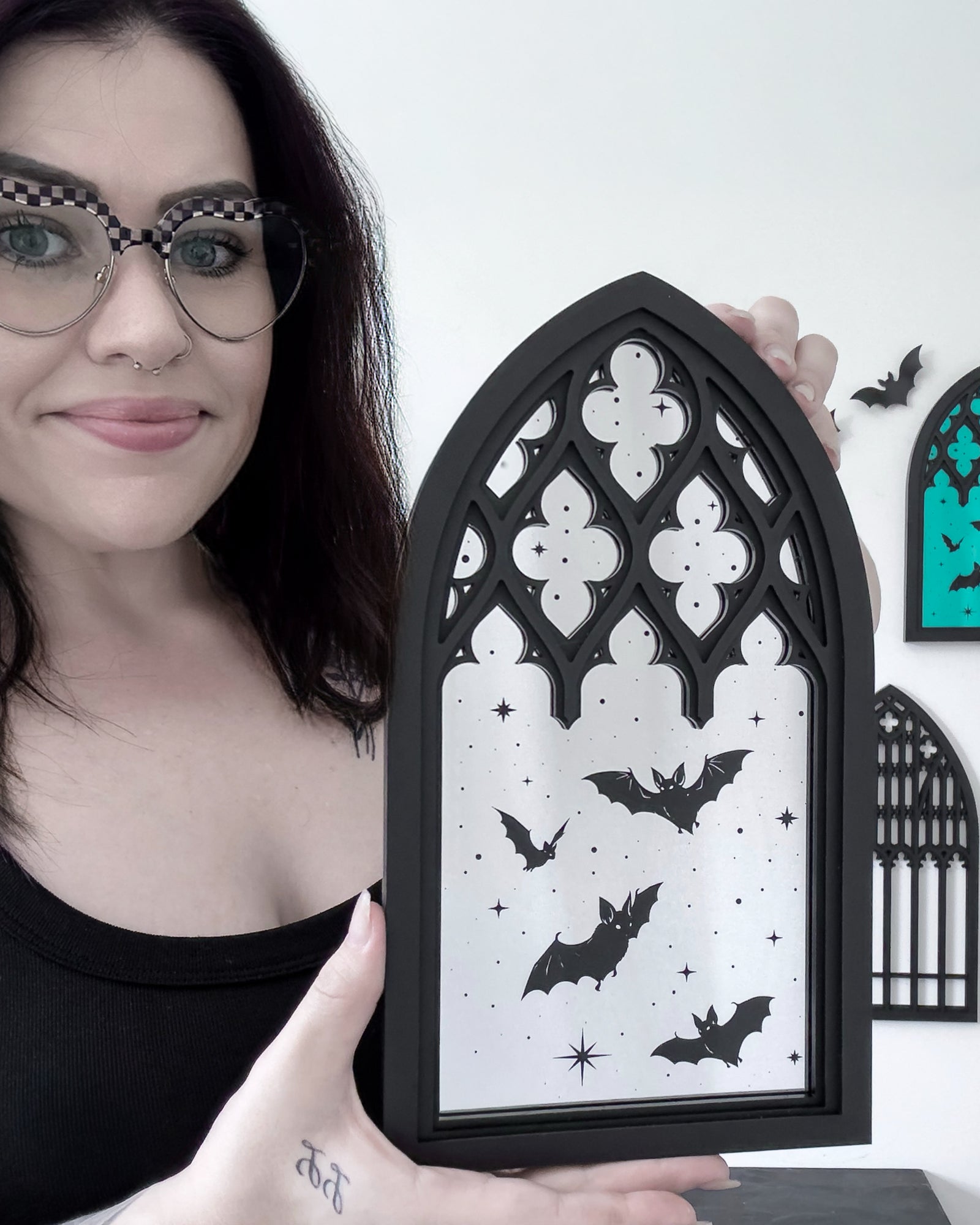 Shannon, founder and maker behind Whispers of the Crypt, holding a bat cathedral wall art piece