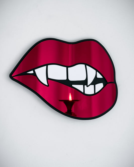 Vampire lips mirror in red acrylic with fangs, reflecting candlelight on a white wall