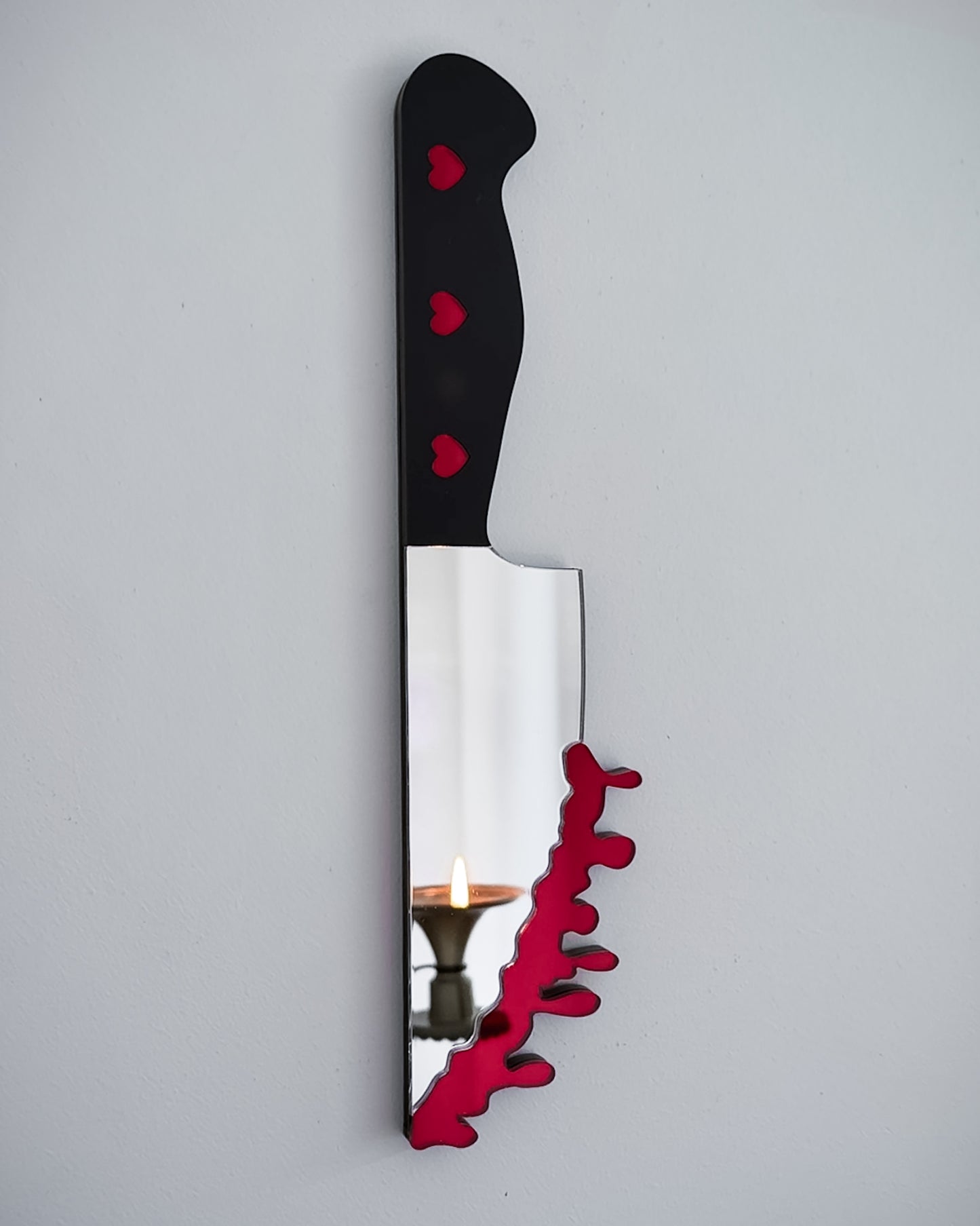 Bloody knife mirror wall art with heart handle and candle reflection on white wall