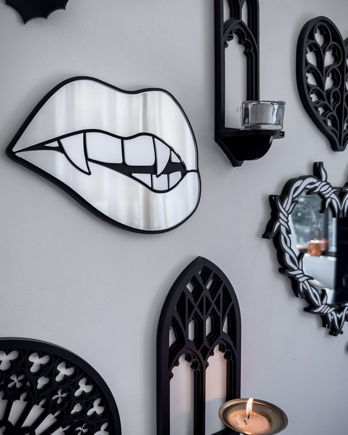 Side view of Silver mirror vampire lips wall art styled on a gothic gallery wall with black bats, cathedral shelf, and candlelight
