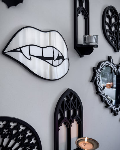 Side view of Silver mirror vampire lips wall art styled on a gothic gallery wall with black bats, cathedral shelf, and candlelight