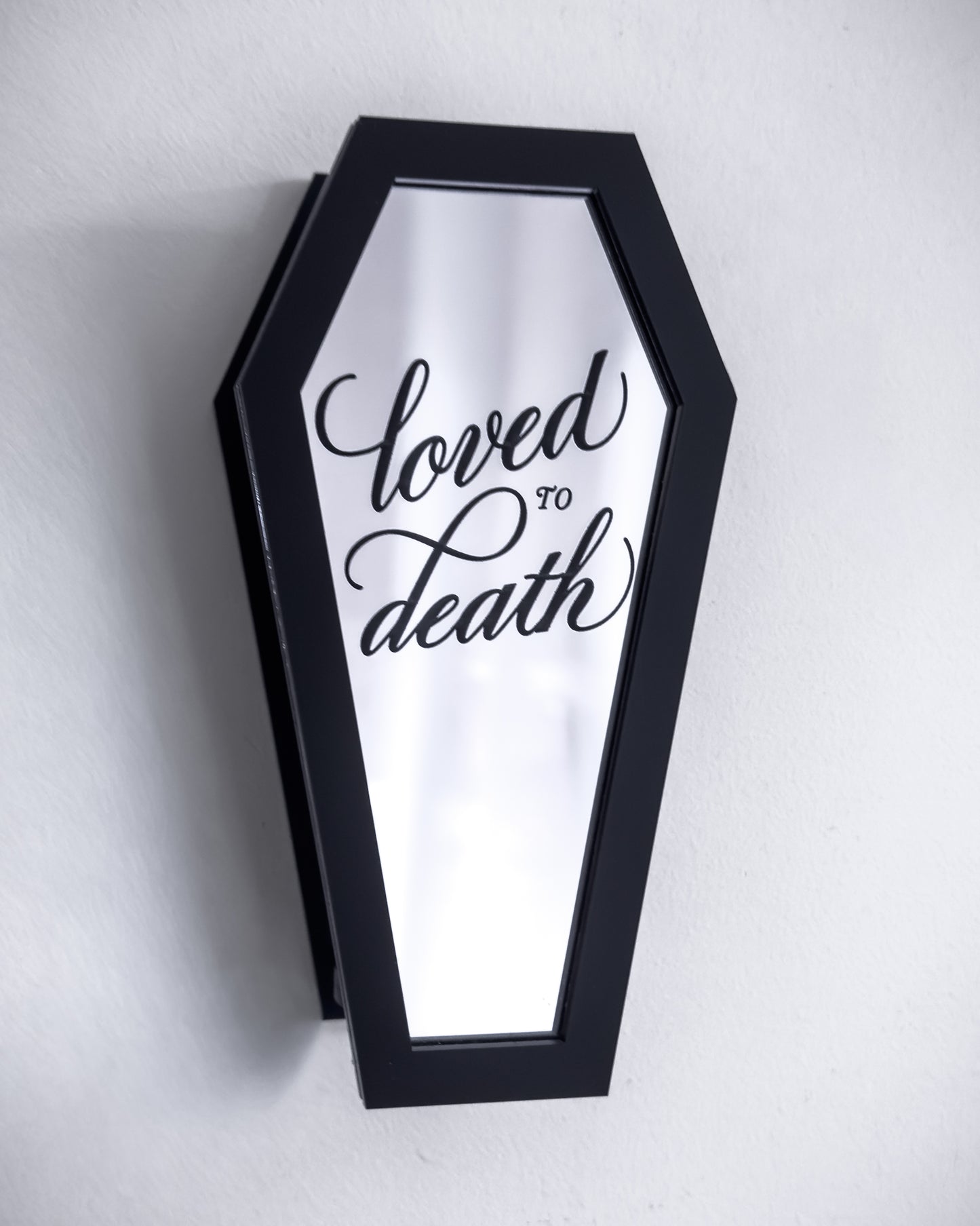 Black coffin-shaped wall propagation vase with engraved mirror front on white wall