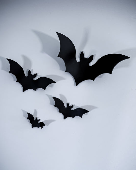 Black acrylic bat wall art set with four flying bats casting shadows on a white wall