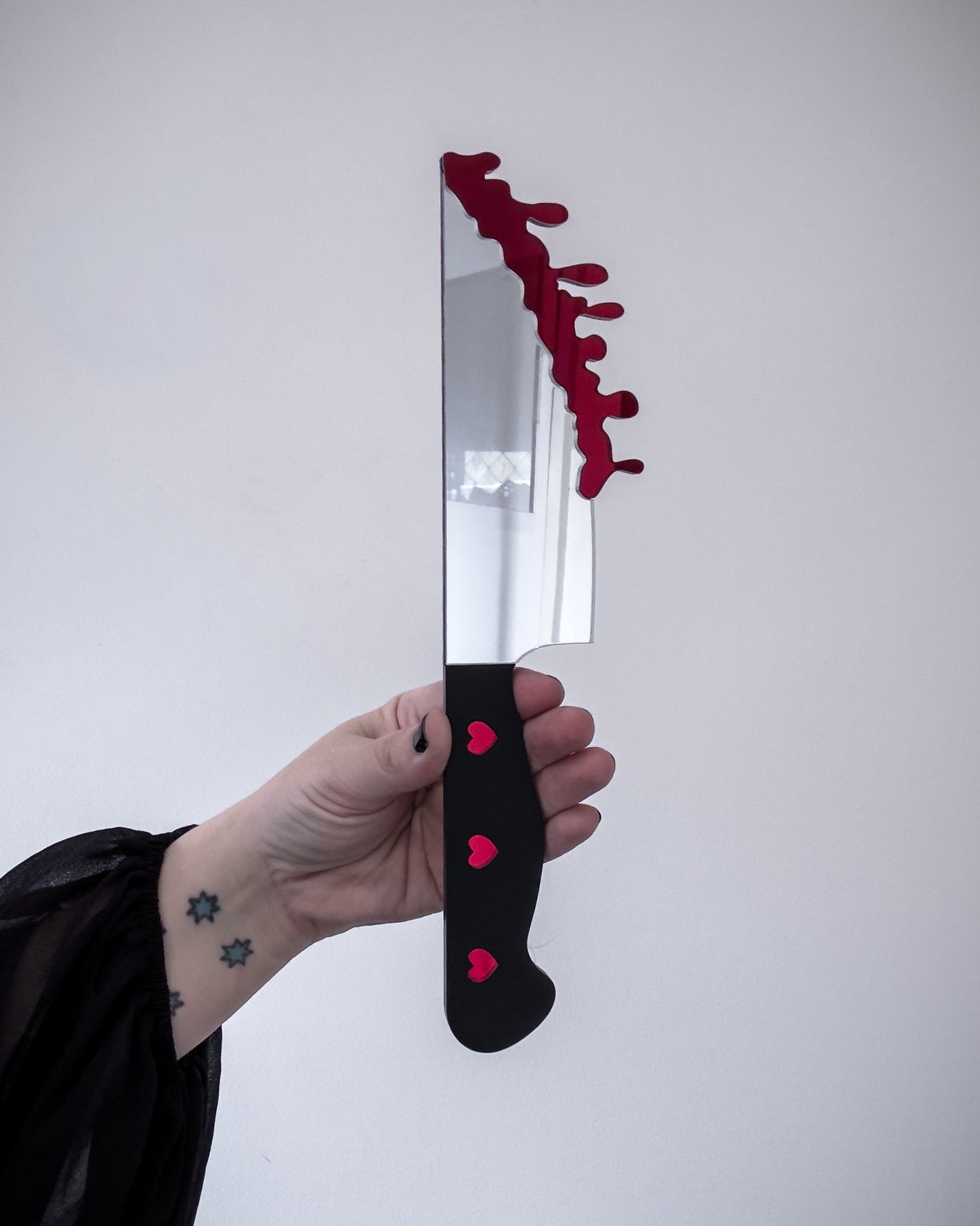 Bloody knife mirror wall art with black handle and red drip detail held in hand for scale