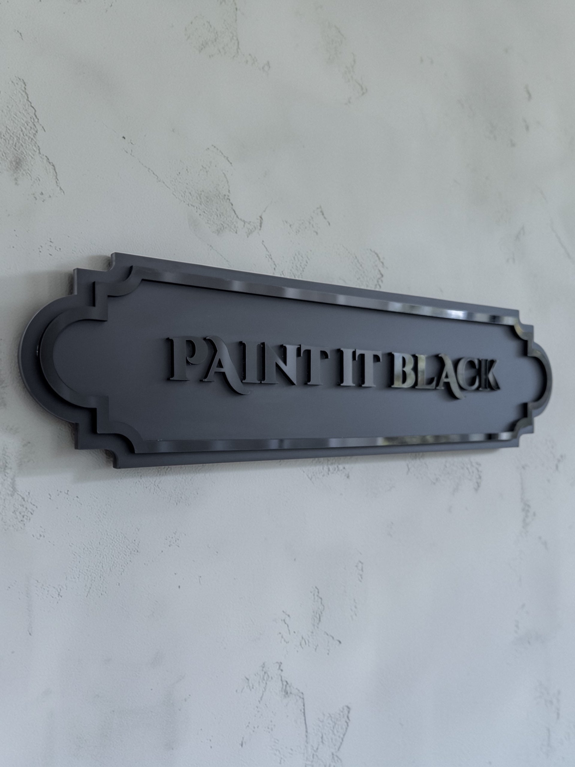 Angled view of paint it black gothic wall art plaque on textured grey wall
