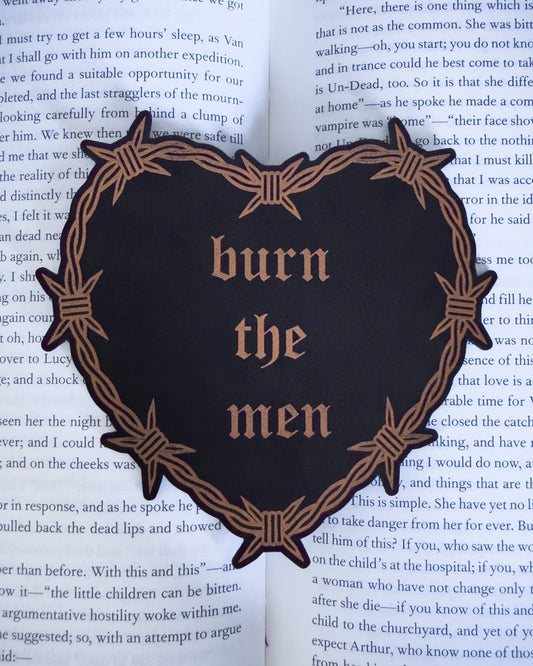 Barbed wire heart bookmark with “burn the men” text in black and copper leatherette, resting on an open book