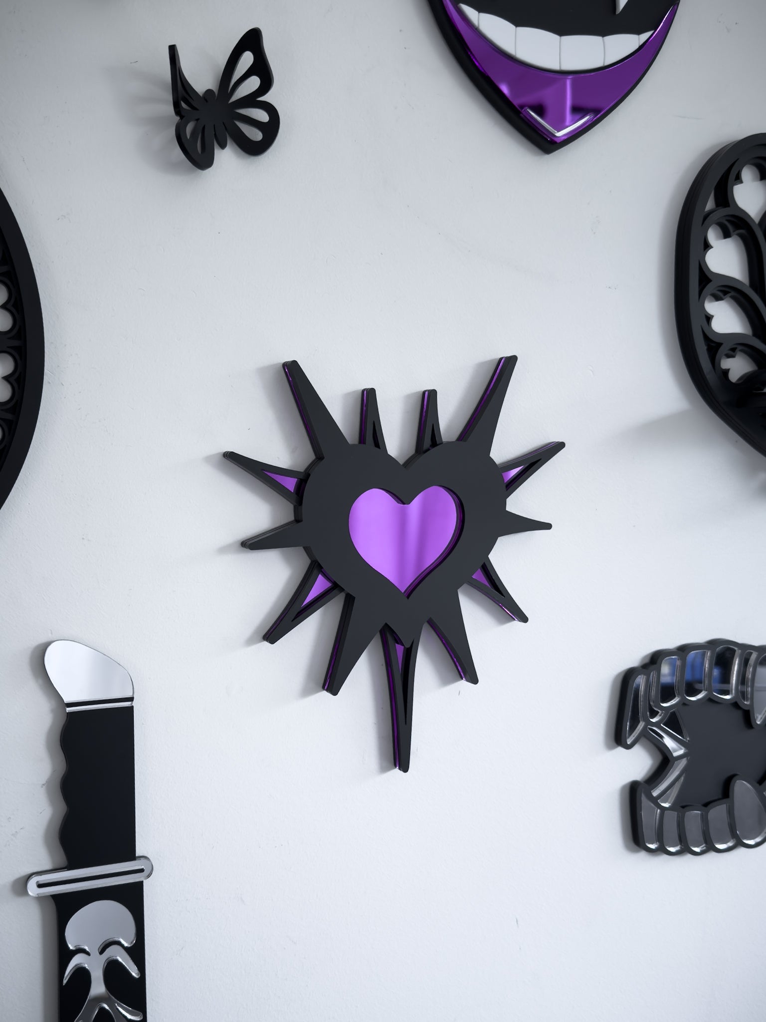 Close-up of gothic gallery wall featuring purple barbed heart wall art  mirror with knife decor and butterfly accents