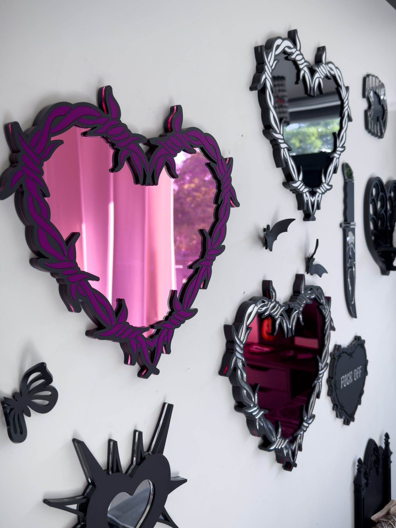 Side view of Gallery wall featuring barbed wire heart mirrors in pink, silver and red acrylic