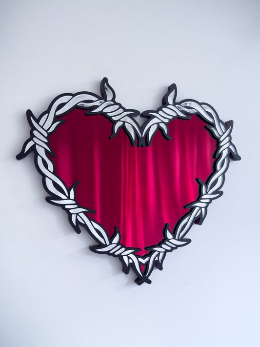 Close-up of silver and red  barbed wire heart mirror in layered acrylic gothic wall decor on a white wall