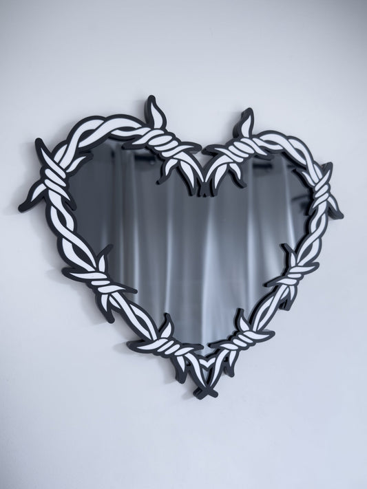 Close-up of white and smoke barbed wire heart mirror in layered acrylic gothic wall decor on a white wall
