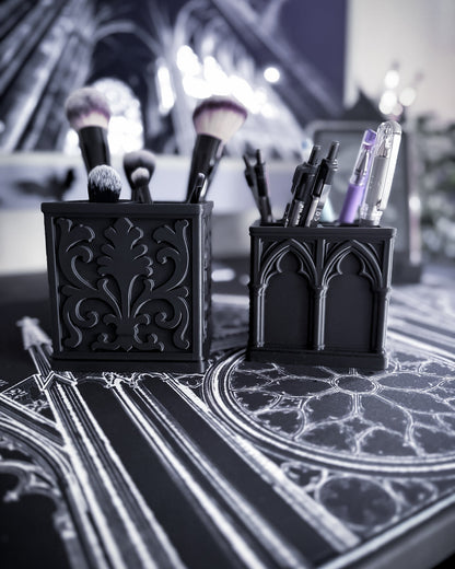 Black baroque organisers with gothic detailing holding makeup brushes and pens with a cathedral interior in background