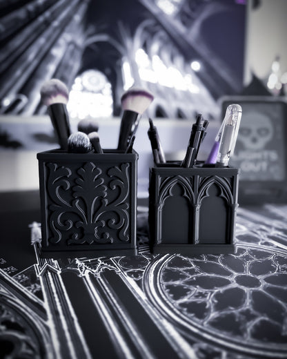 Black baroque organisers with gothic detailing holding makeup brushes and pens, cathedral interior in the background