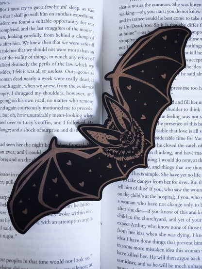 Gothic bat bookmark in black and copper leatherette with heart detail, resting on an open book