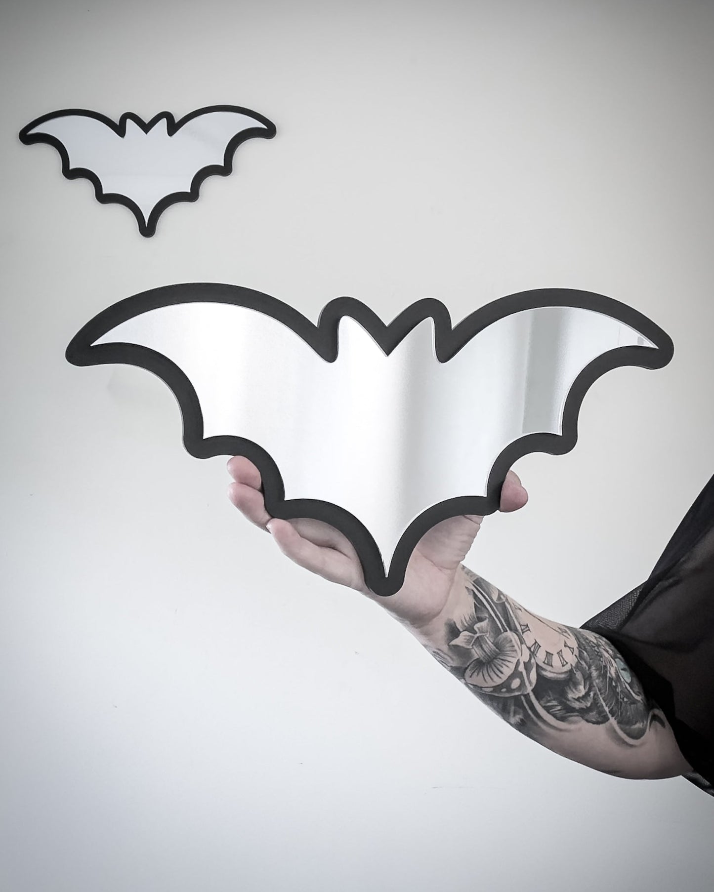 Silver bat mirror wall art with black acrylic frame held for scale