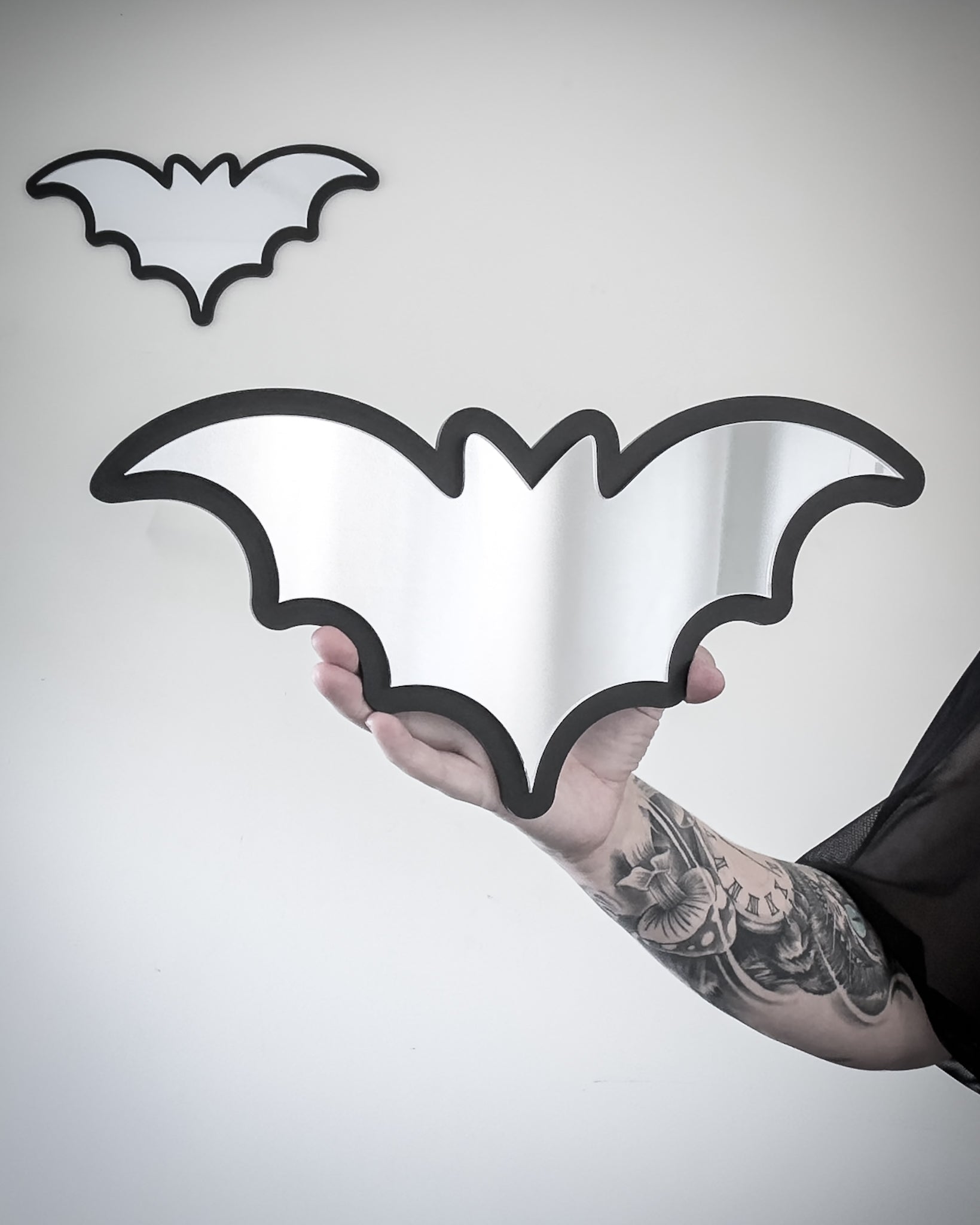 Silver bat mirror wall art with black acrylic frame held for scale