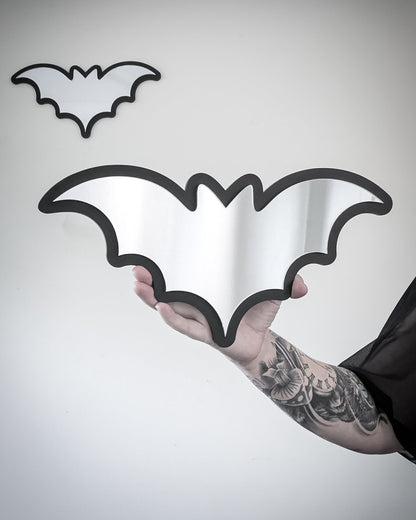Silver bat mirror wall art with black acrylic frame held for scale