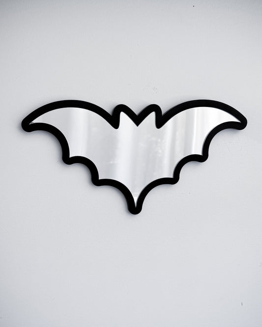 Silver bat mirror wall art with black acrylic frame on a white wall