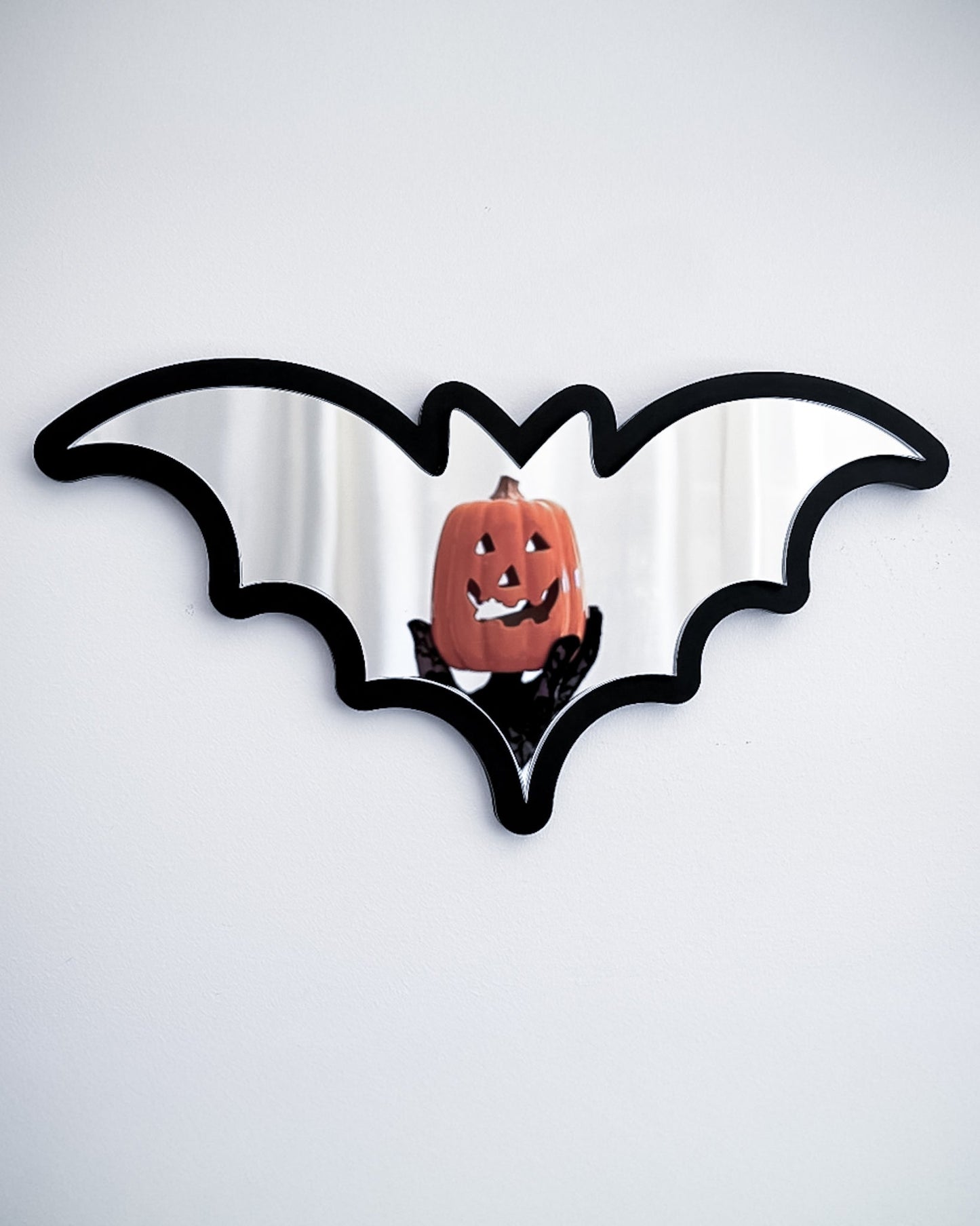 Silver bat mirror wall art reflecting a pumpkin decoration on a white wall