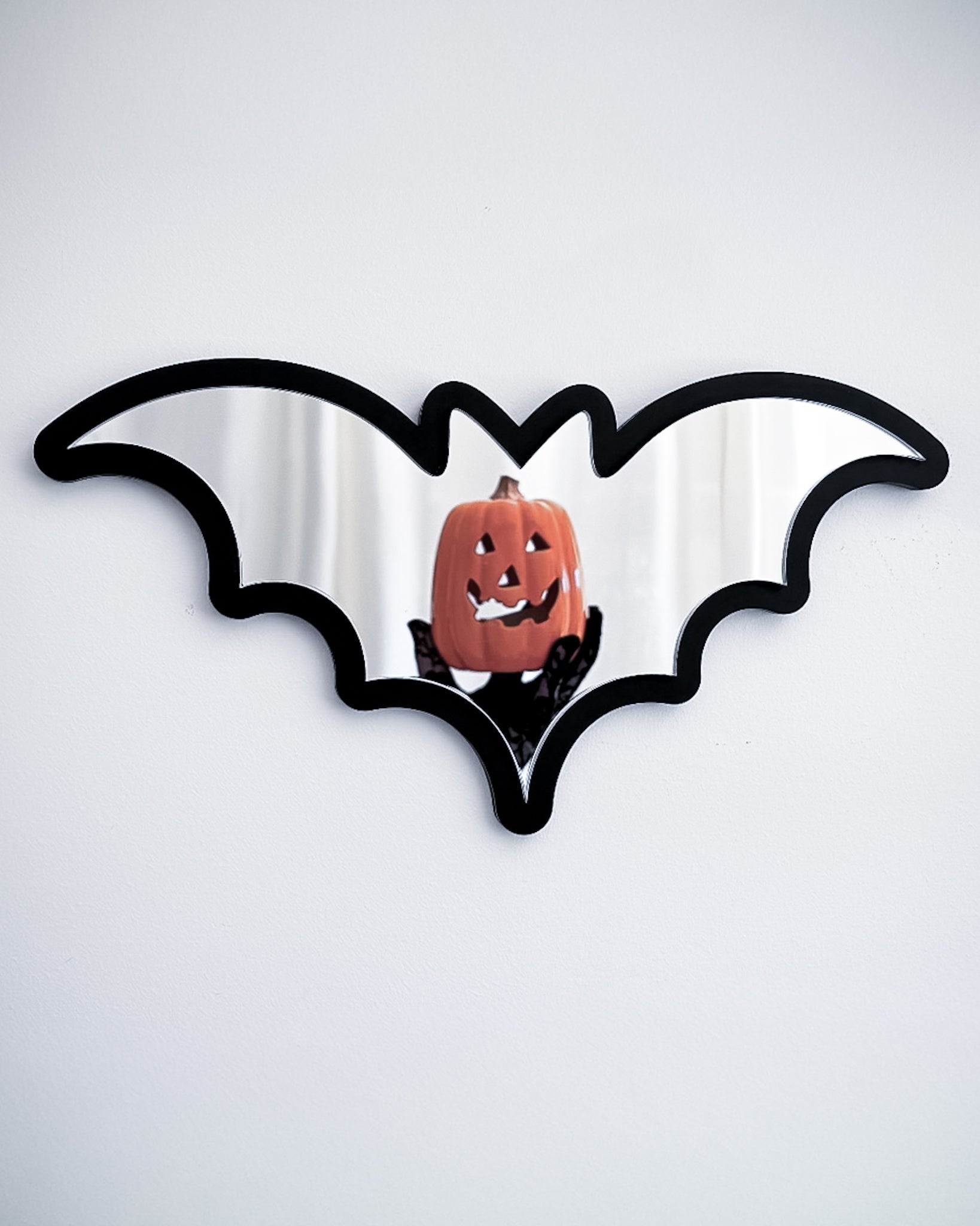 Silver bat mirror wall art reflecting a pumpkin decoration on a white wall