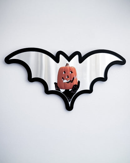 Silver bat mirror wall art reflecting a pumpkin decoration on a white wall