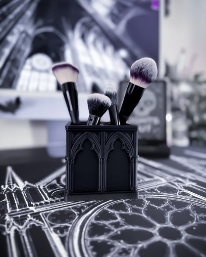 Black cathedral desk organiser with gothic arch detailing holding makeup brushes on a table, cathedral interior in the background