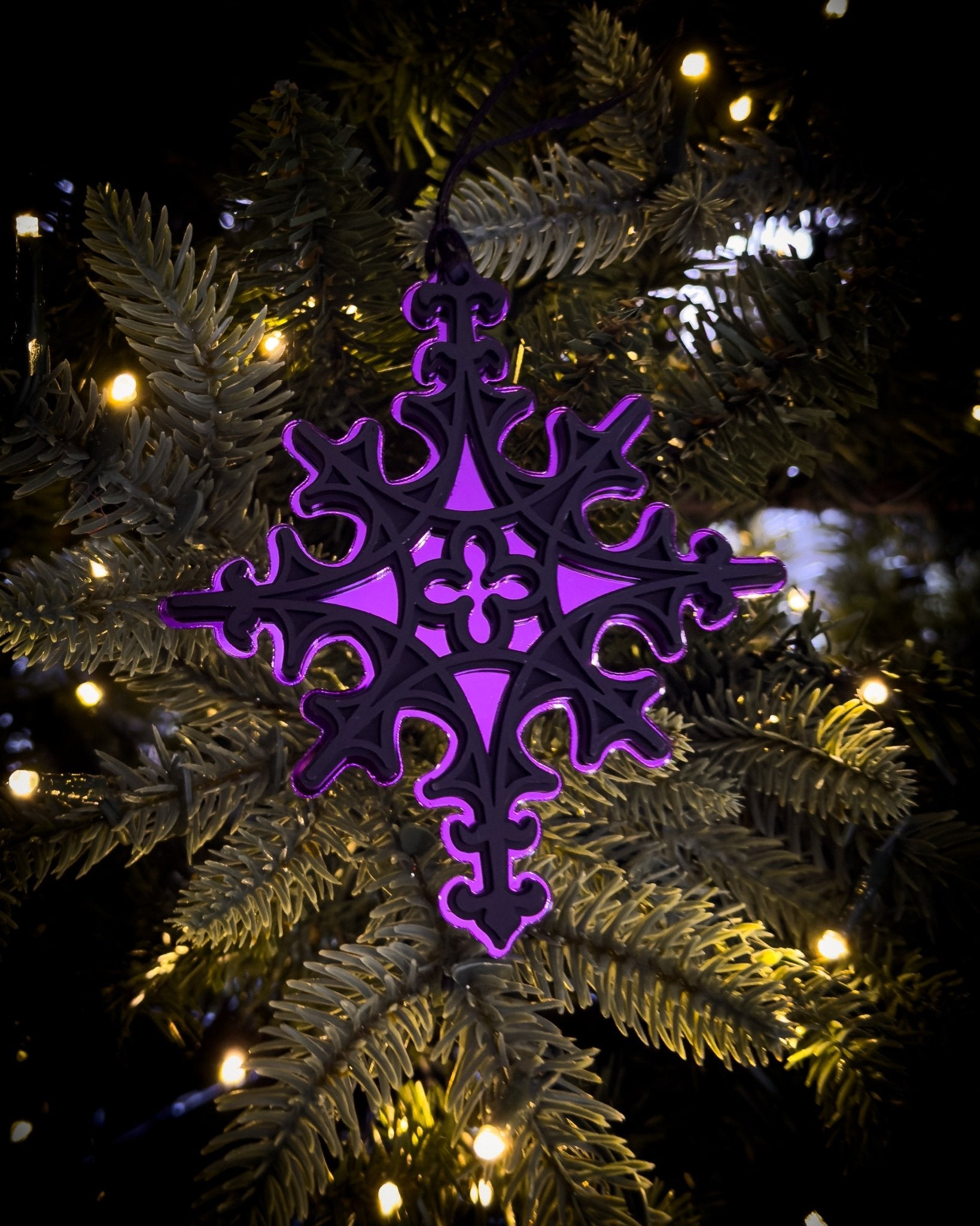 Purple gothic cathedral star ornament hanging on Christmas tree with warm lights