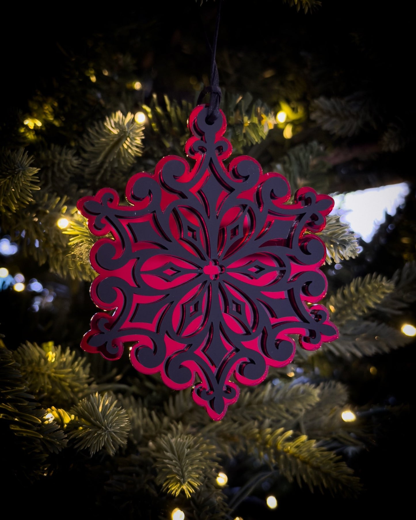 Red gothic cathedral snowflake ornament hanging on Christmas tree with warm lights
