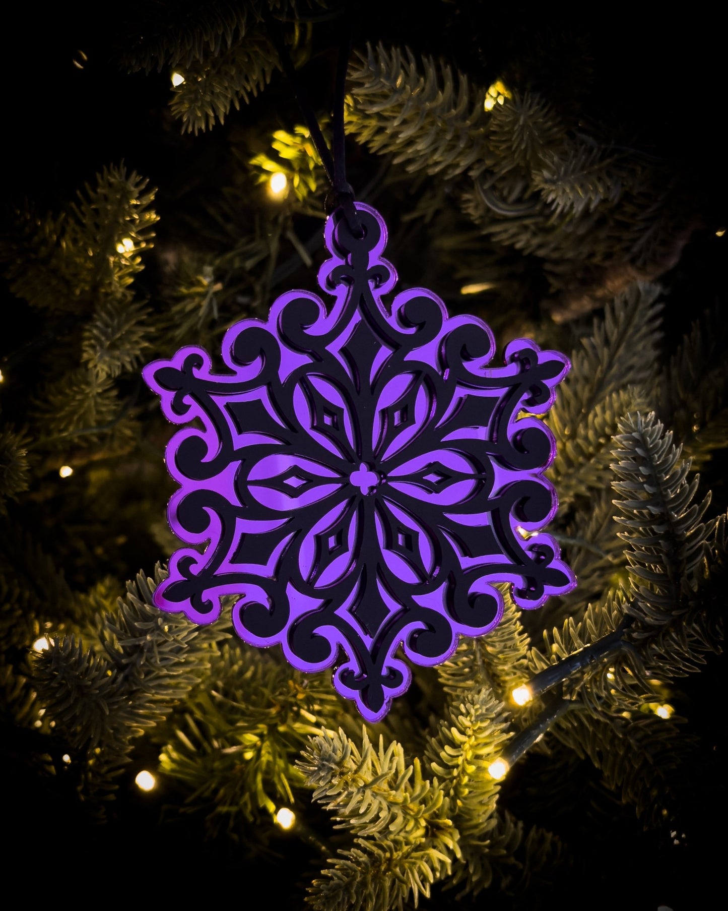 Purple gothic cathedral snowflake ornament hanging on Christmas tree with warm lights