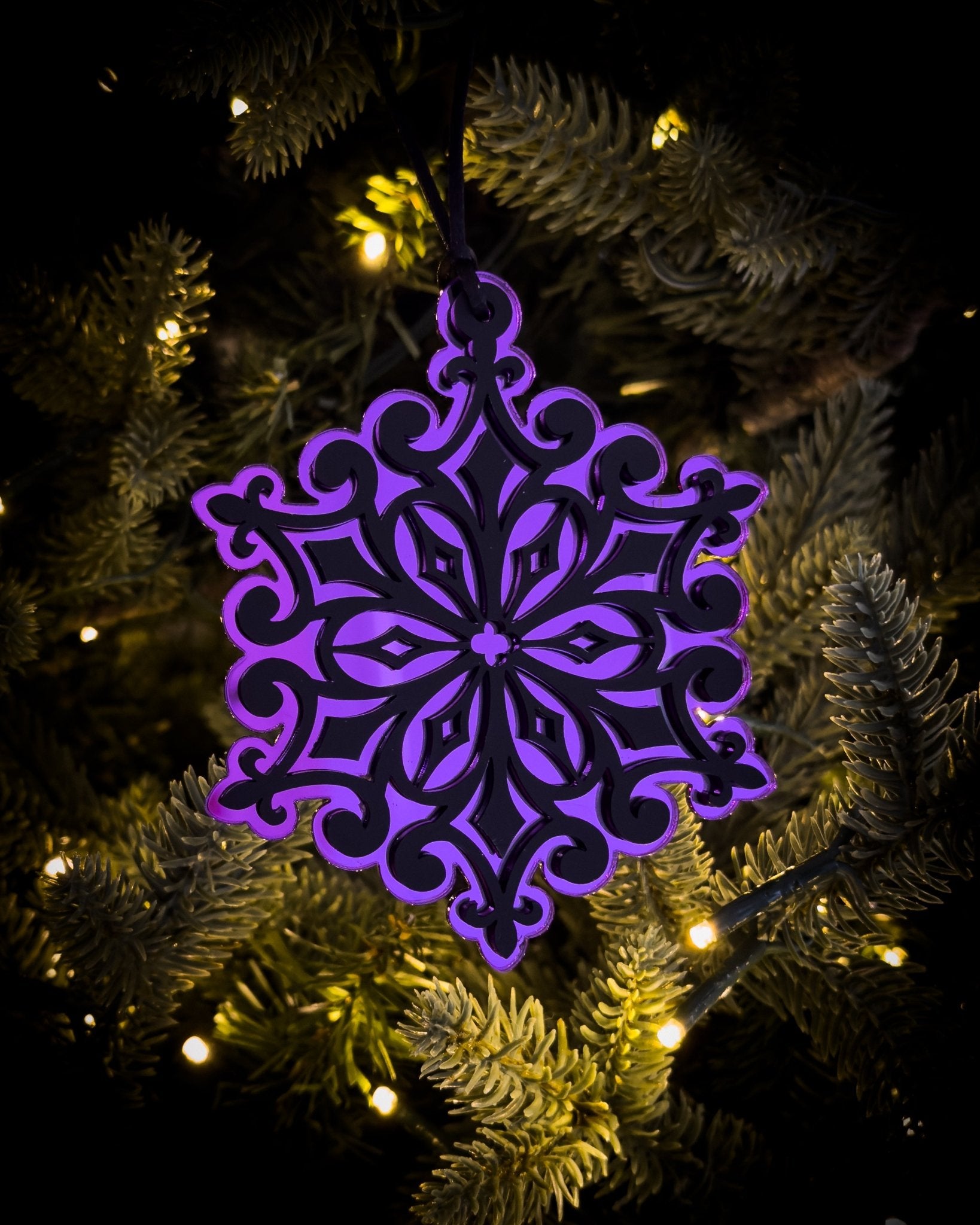 Purple gothic cathedral snowflake ornament hanging on Christmas tree with warm lights
