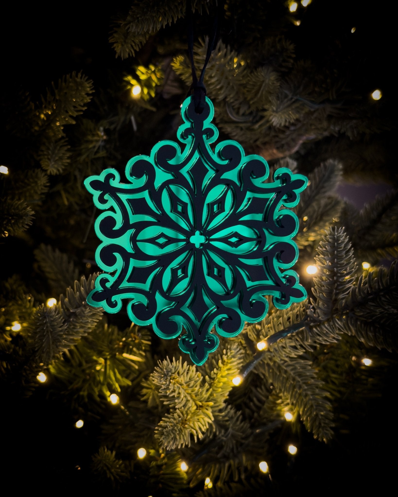 Green gothic cathedral snowflake ornament hanging on Christmas tree with warm lights