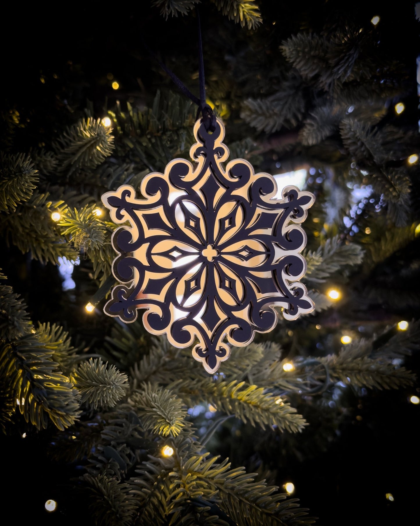 Gold gothic cathedral snowflake ornament hanging on Christmas tree with warm lights