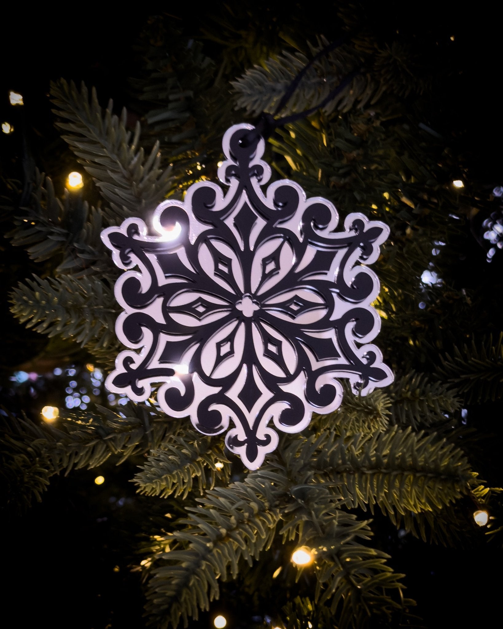 Silver gothic cathedral snowflake ornament hanging on Christmas tree with warm lights