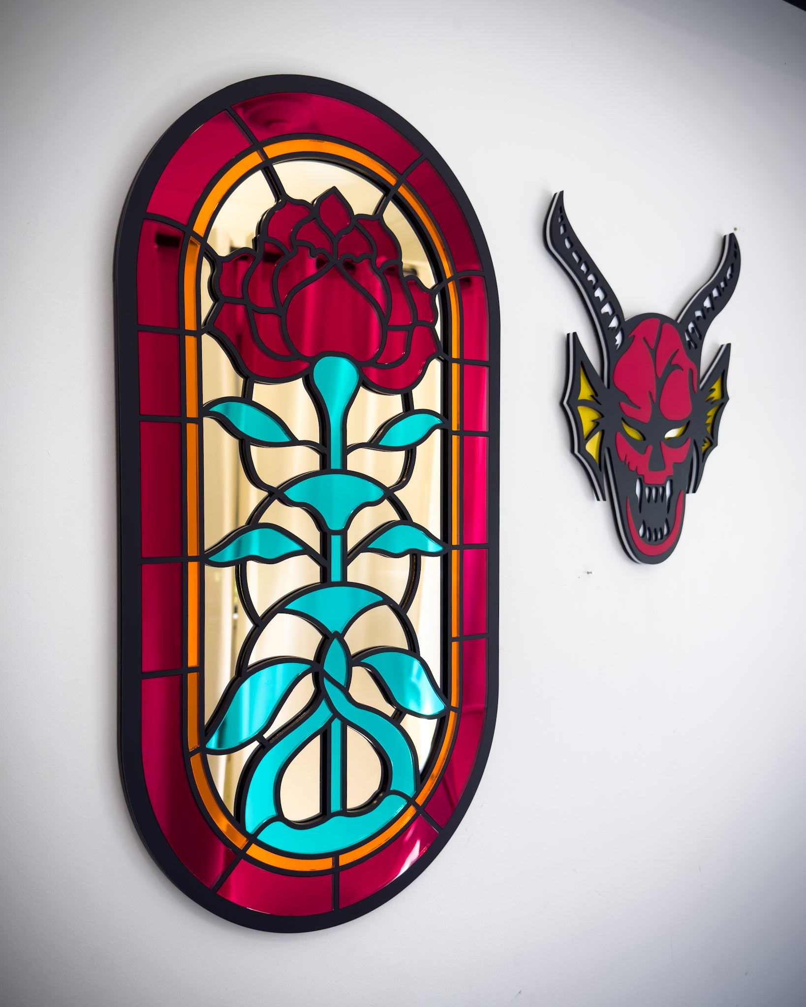 Side view of Gothic stained glass rose window mirror displayed beside red hellfire demon wall art on a white wall