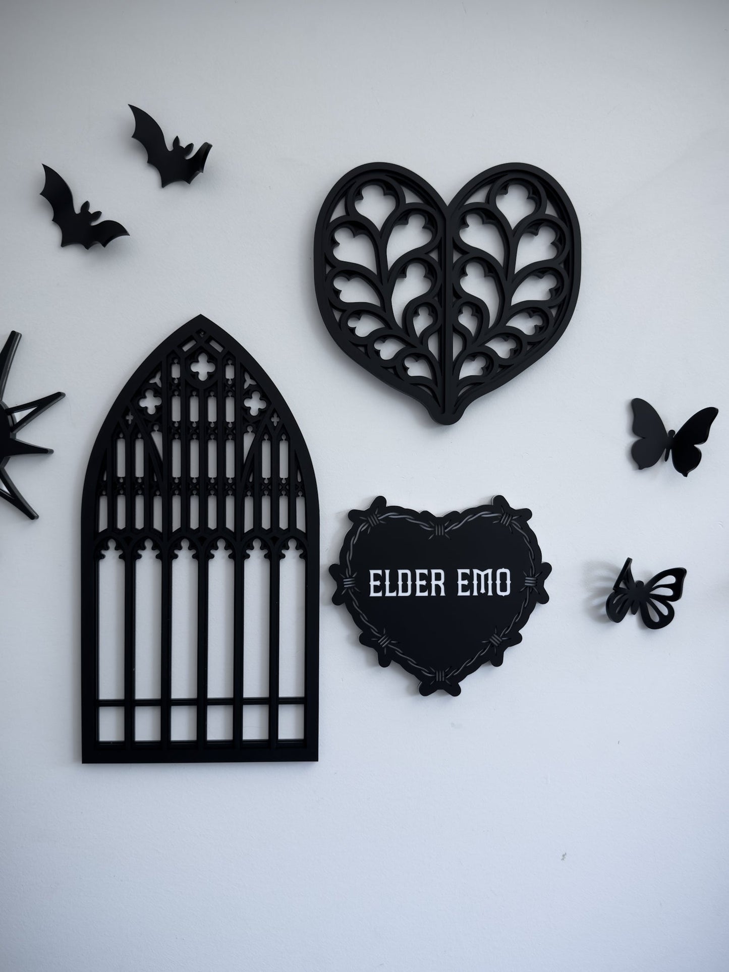 Gothic gallery wall with cathedral window wall art, barbed wire heart “Elder Emo” sign and bat decor