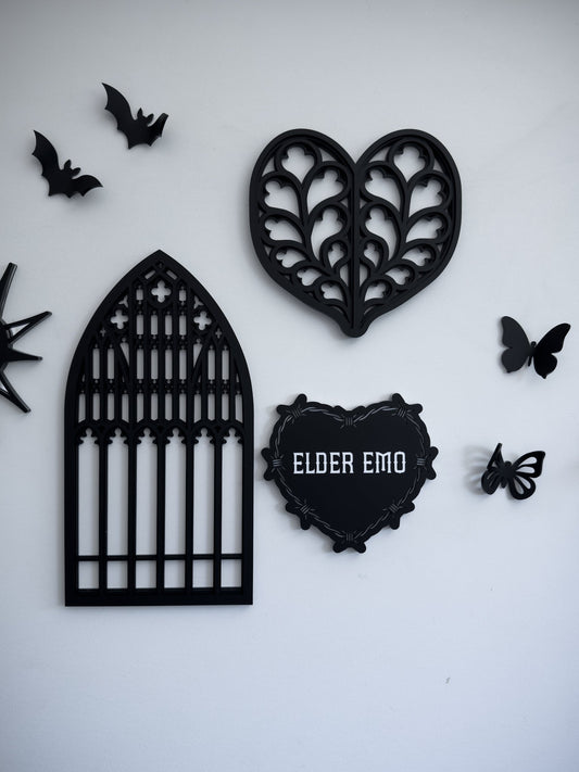 Gothic gallery wall with cathedral window wall art, barbed wire heart “Elder Emo” sign and bat decor