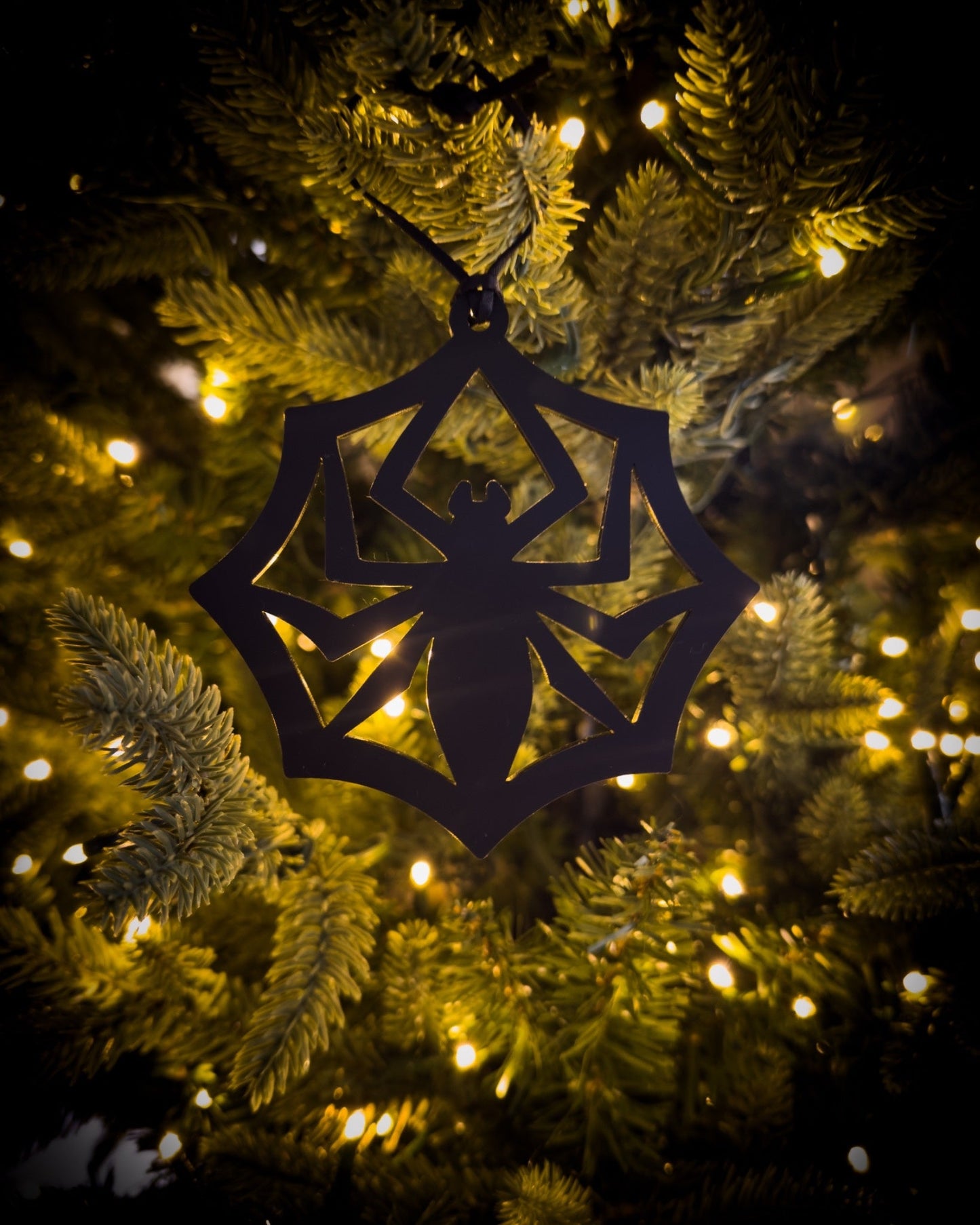 Black acrylic, gothic spider web ornament hanging on Christmas tree with warm lights