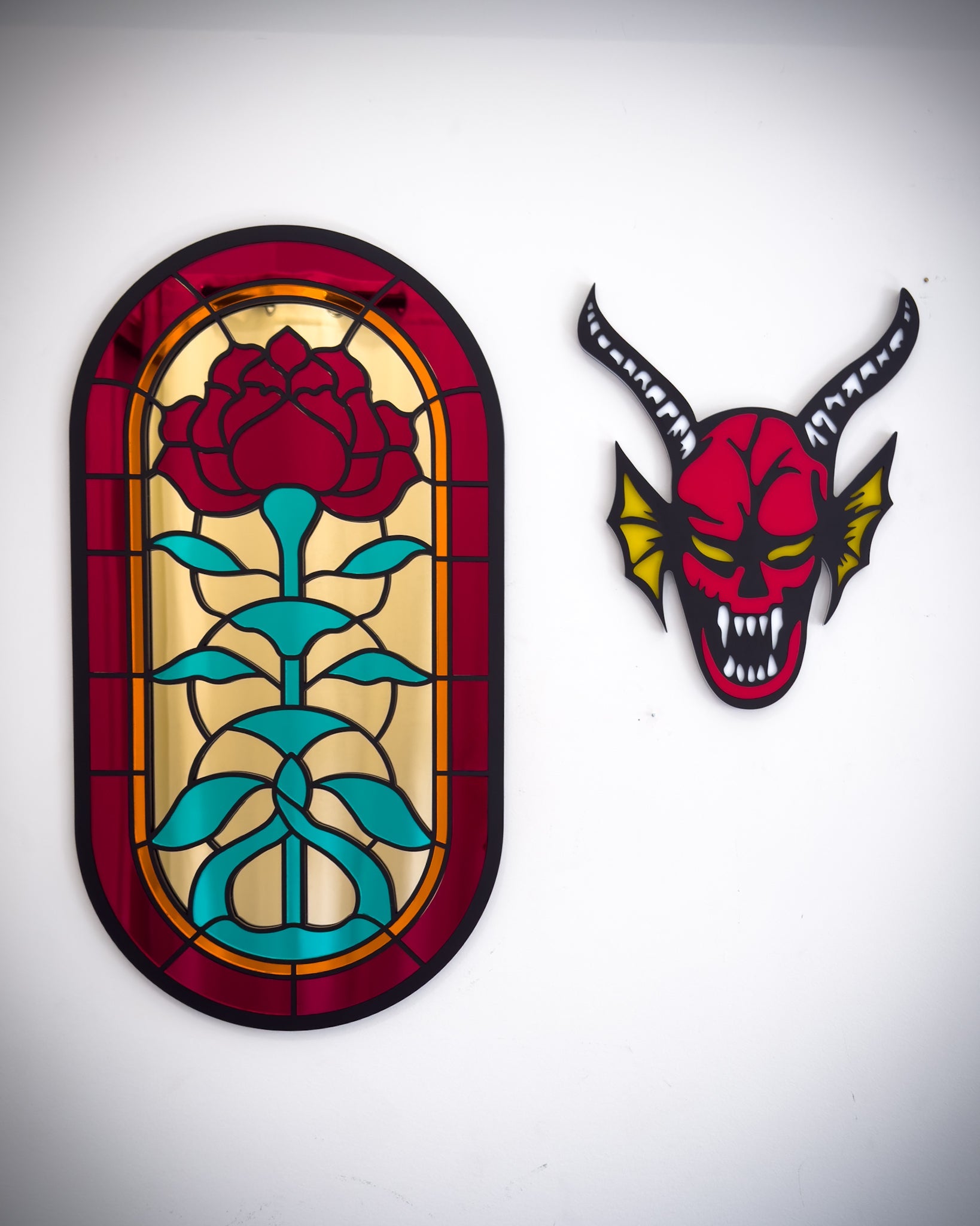 Large gothic stained glass style rose window mirror shown beside red and black hellfire demon acrylic wall art