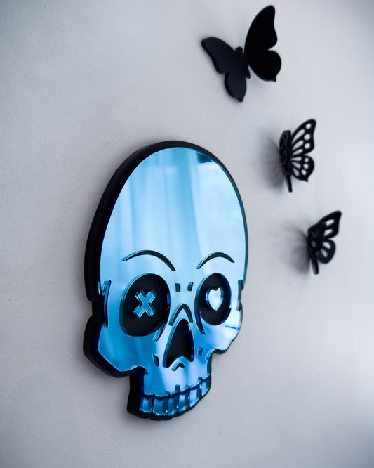 Close-up side view of blue skull mirror with mismatched heart and X eyes and 3d butterflies on a white wall
