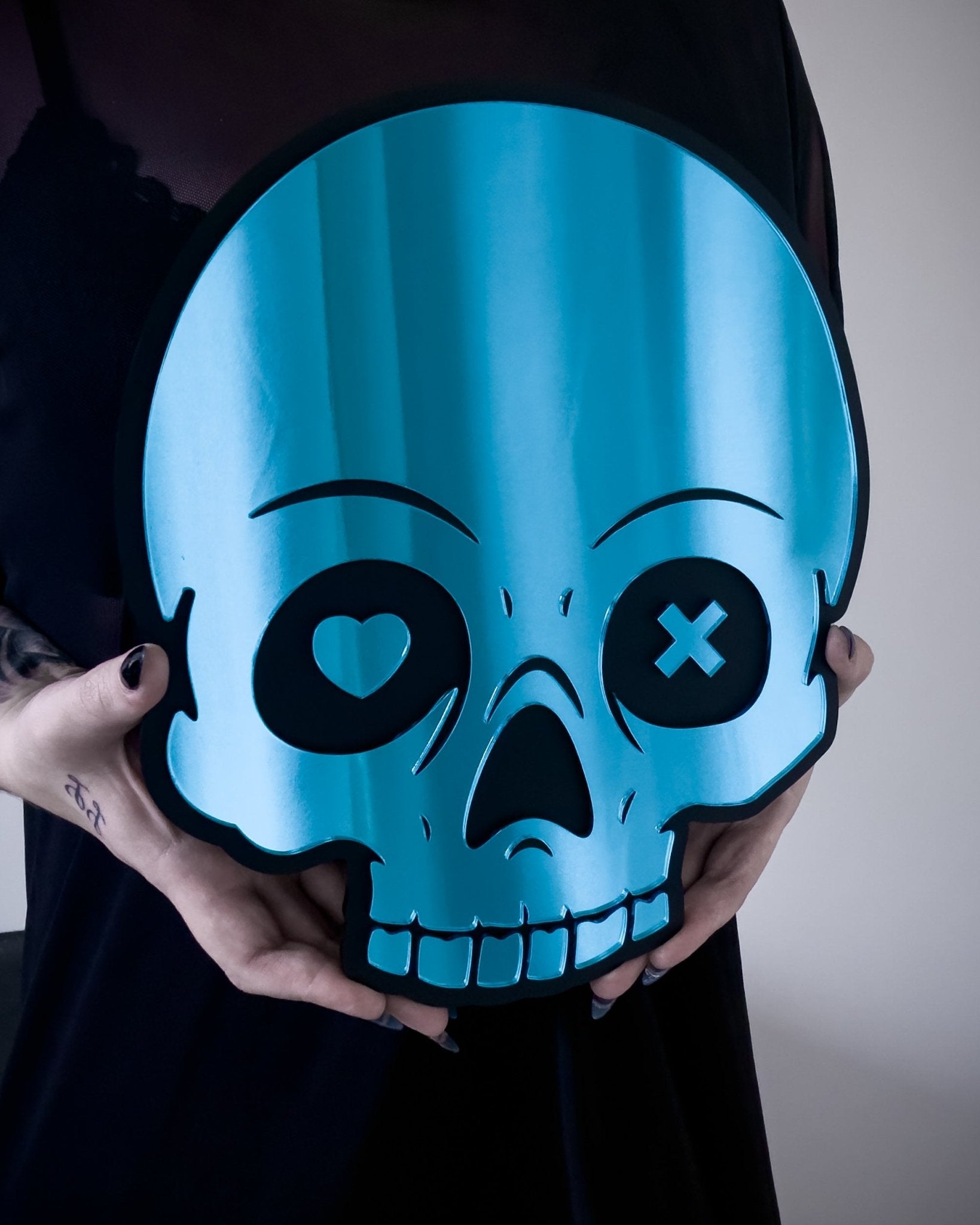 Close-up of blue skull mirror with heart and X eyes held by person for size reference