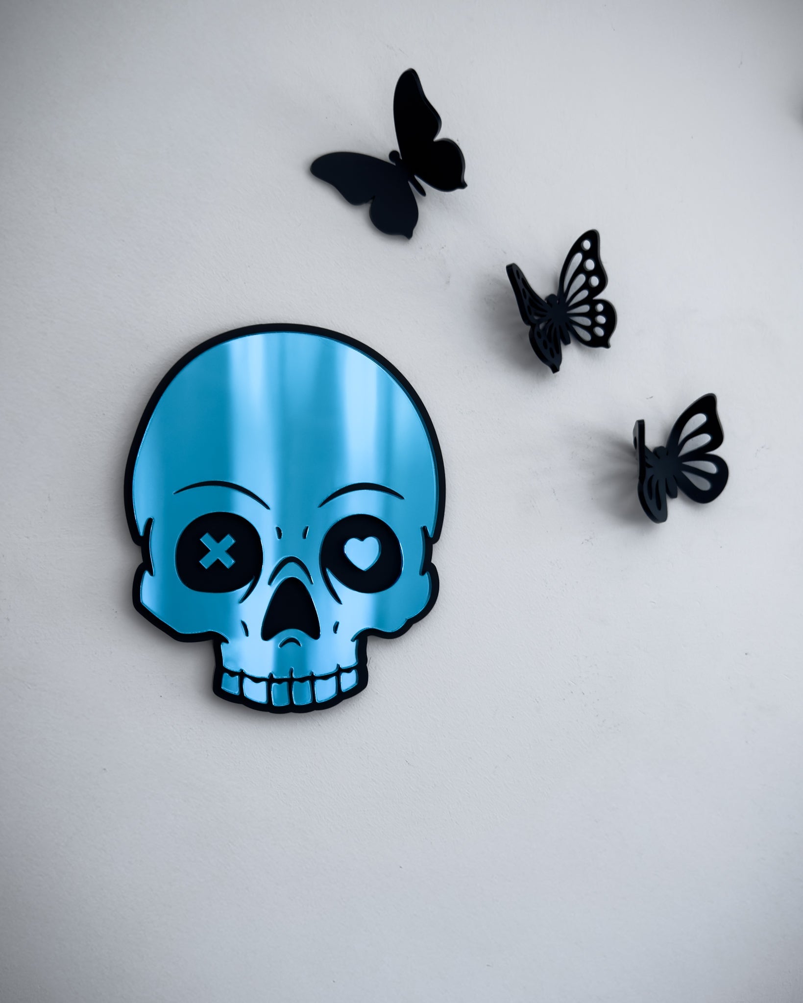 Bue skull mirror with mismatched heart and X eyes and 3d butterflies on a white wall