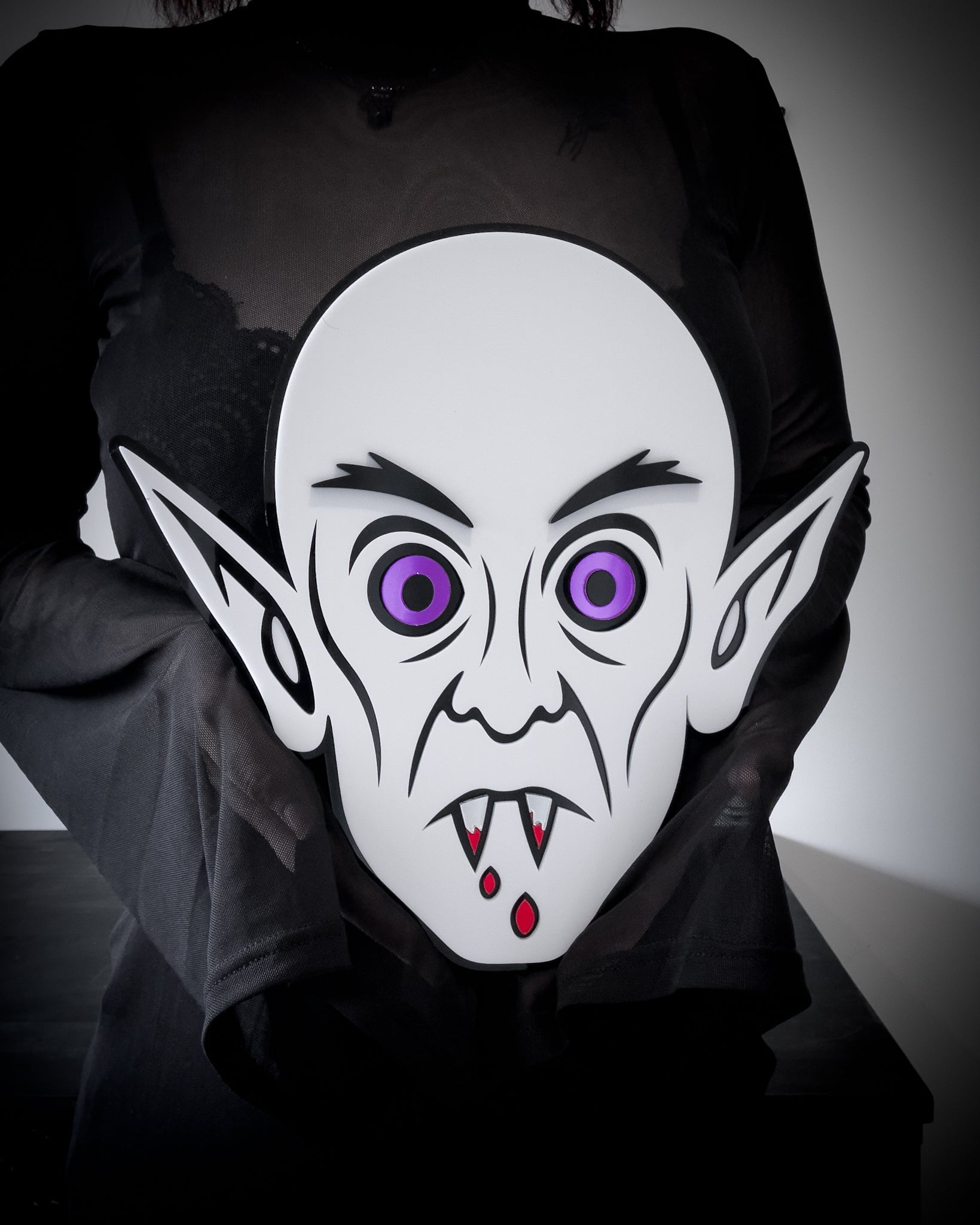 White Nosferatu wall art with purple eyes and blood detail, held for size reference