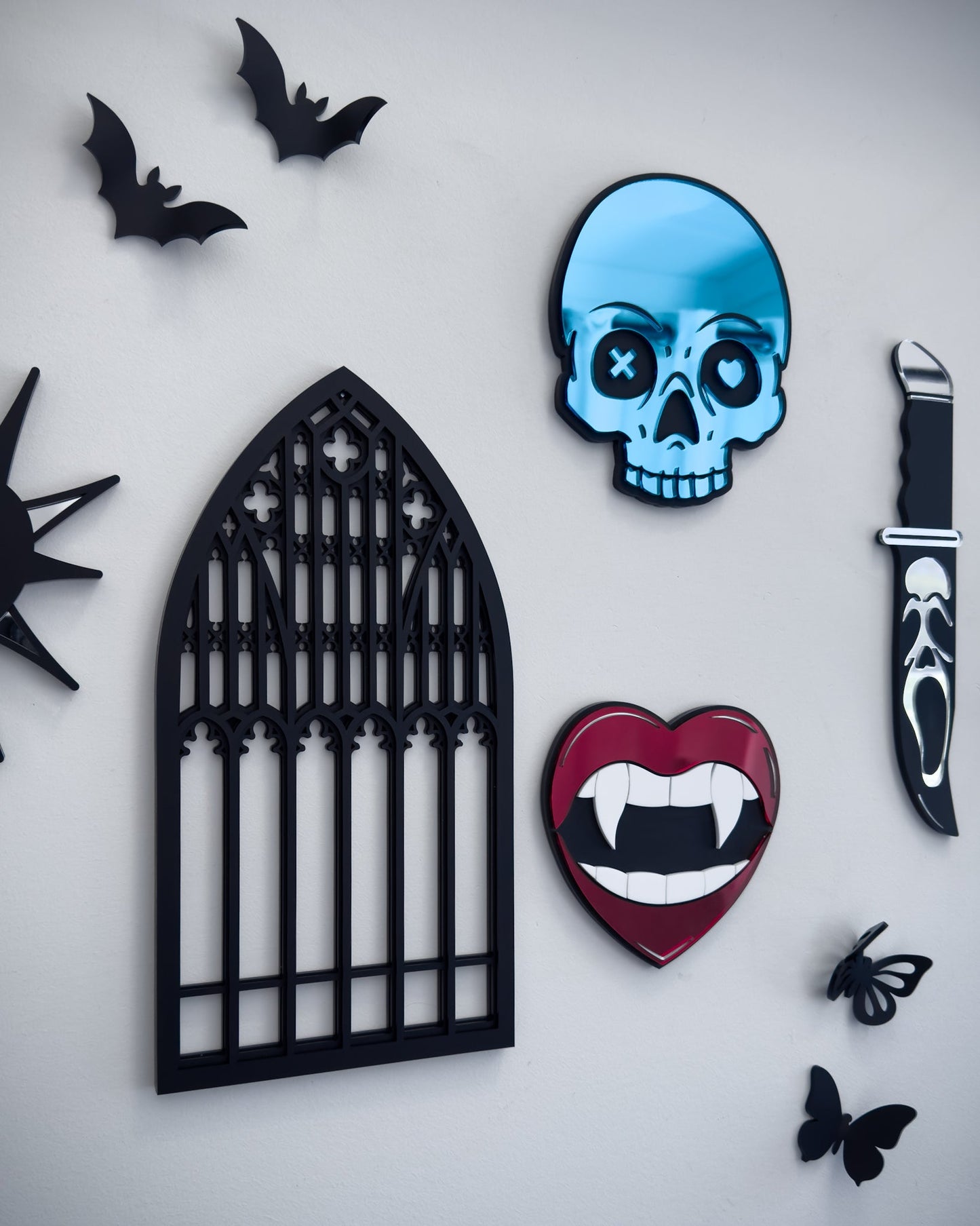 Side view of gothic gallery wall featuring Salem cathedral window wall art, blue skull mirror, vampire lips mirror, Ghostface knife mirror and 3d bats