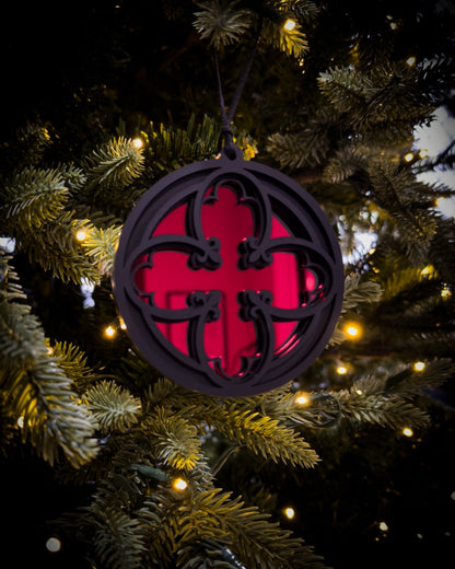 Red gothic cathedral quatrefoil ornament hanging on Christmas tree with warm lights