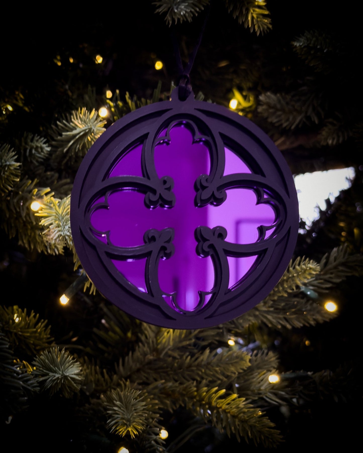 Purple gothic cathedral quatrefoil ornament hanging on Christmas tree with warm lights